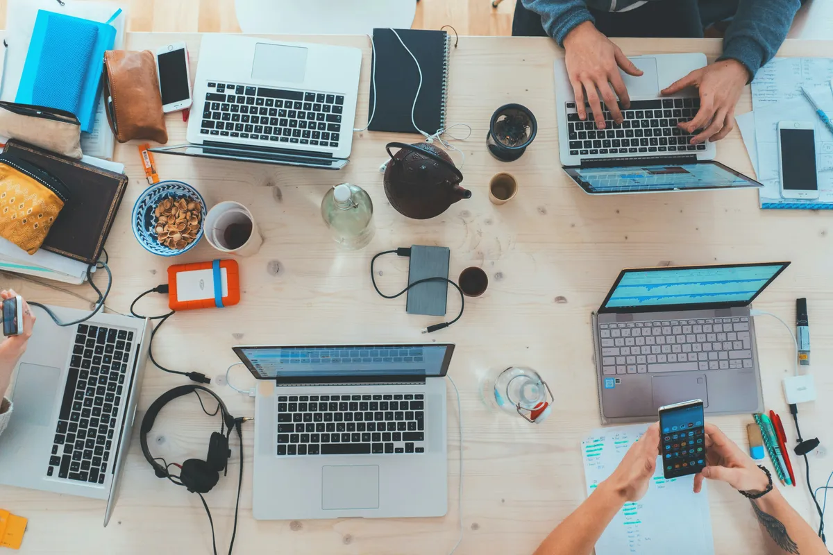Overhead view of a team working at a shared table with laptops, phones and notebooks.