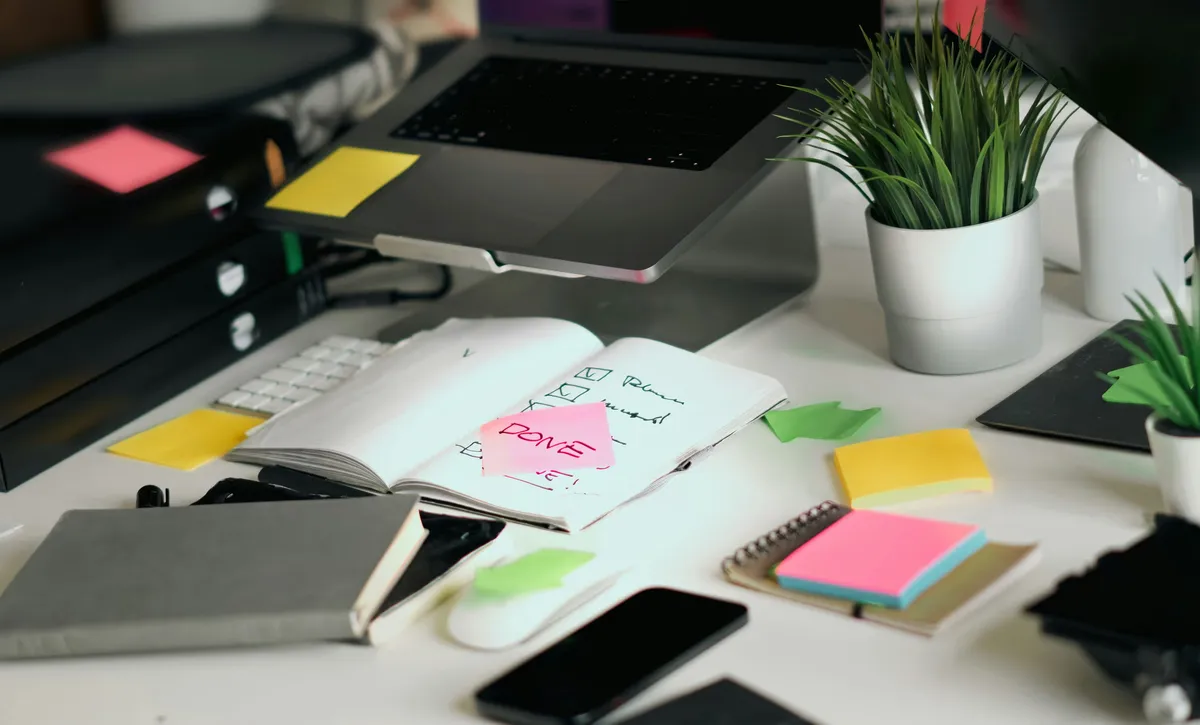 Desk with a laptop, notebook and colorful sticky notes used for planning work.